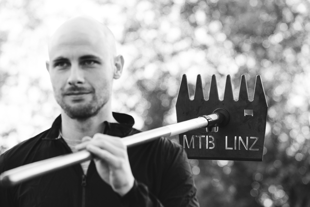 Max Reiser, einer der Wegerhalter von MTB Linz mit den typischen Trailbau-Werkzeugen. Natürlich mit entsprechendem Branding.