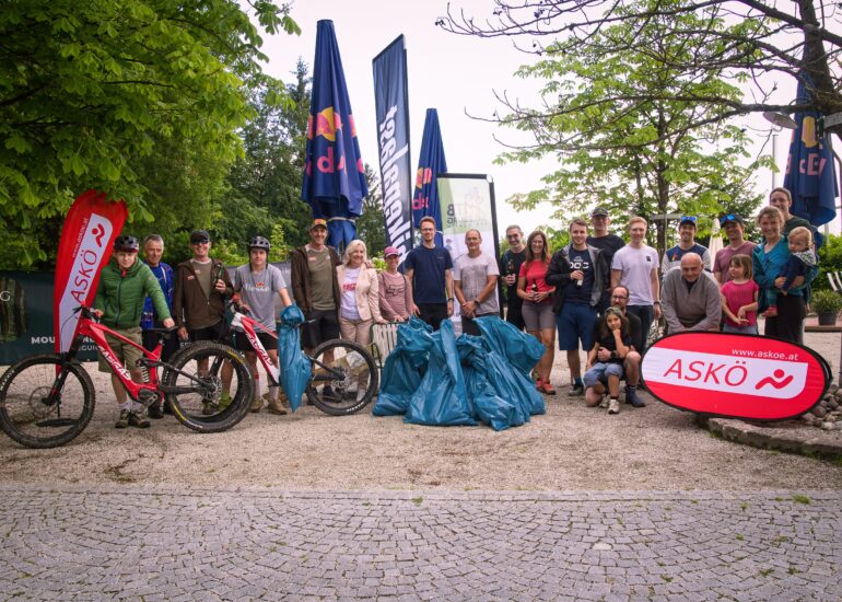 Eine Gruppe Mountainbiker mit aufgestapelten, gefüllten Müllsäcken, die vor ihnen liegen.