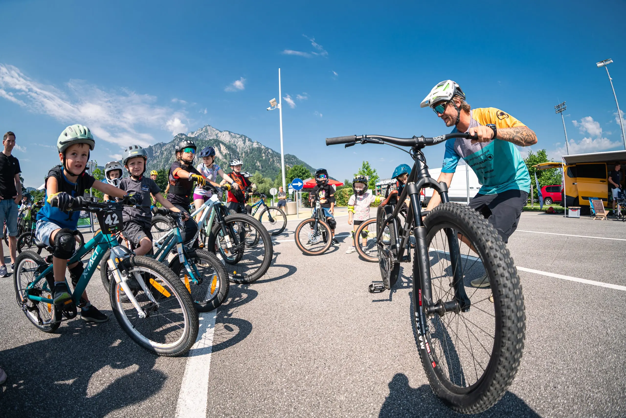 Ein MTB-Guide mit einer Gruppe Kids auf einem Parkplatz.