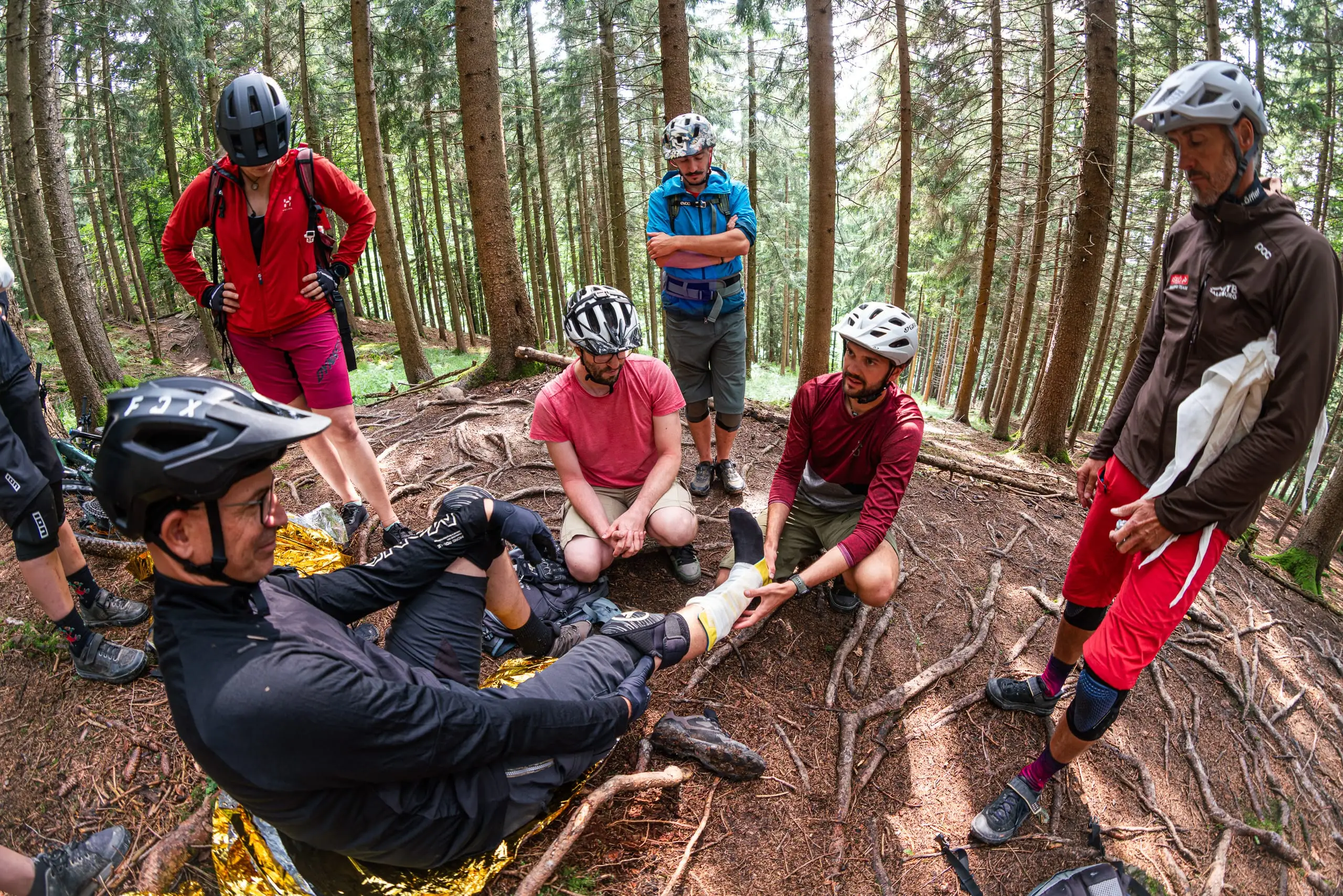 Eine Gruppe Mountainbiker üben auf einem Trail Erste-Hilfe-Maßnahmen.