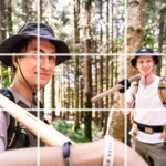 Zwei Trailbauer mit Werkzeugen auf der Schulter lachen in die Kamera.