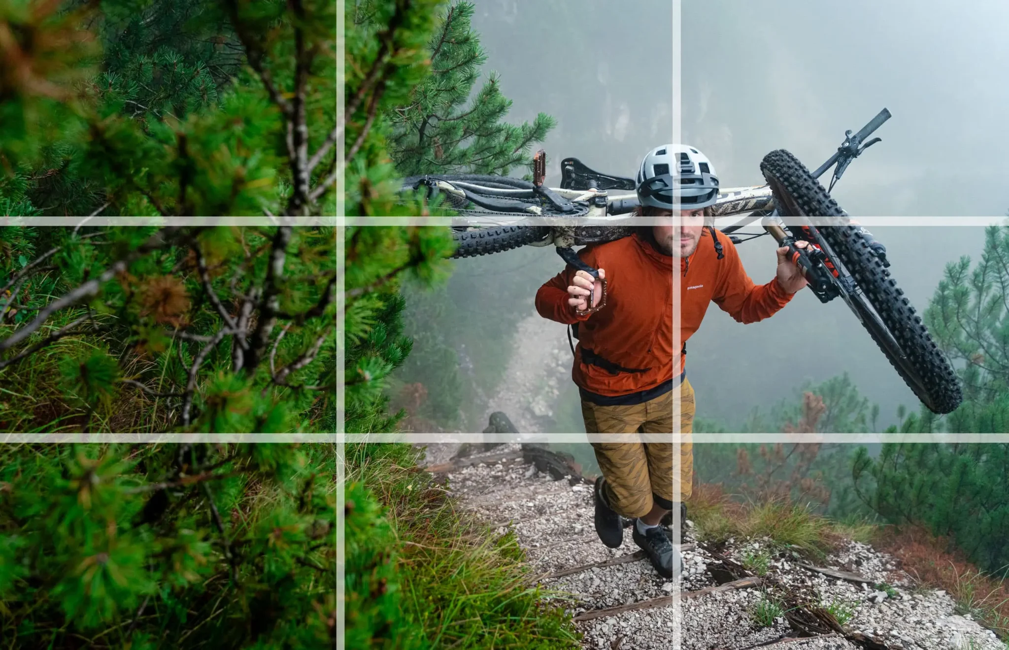 Ein Mountainbiker trägt sein Fahrrad einen schmalen Pfad hinauf. Um die Drittel-Regel zu veranschaulichen, wurde darüber ein Overlay-Gitter gelegt.