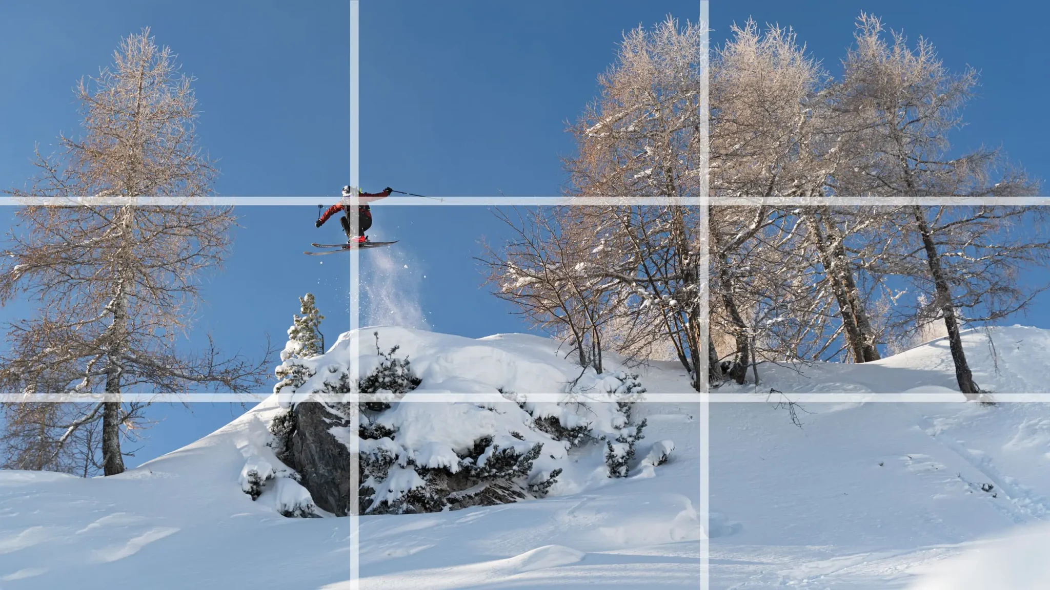 Ein Freerider springt eine Klippe hinunter. Um die Drittel-Regel zu veranschaulichen, wurde darüber ein Overlay-Gitter gelegt.