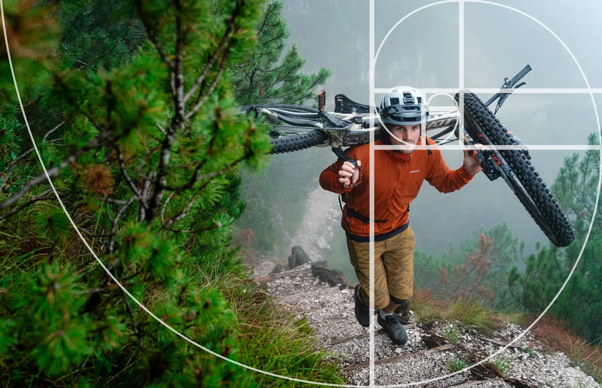Ein Mountainbiker trägt sein Fahrrad einen schmalen Pfad hinauf. Um den Goldenen Schnitt zu veranschaulichen, wurde darüber ein Overlay-Gitter gelegt.